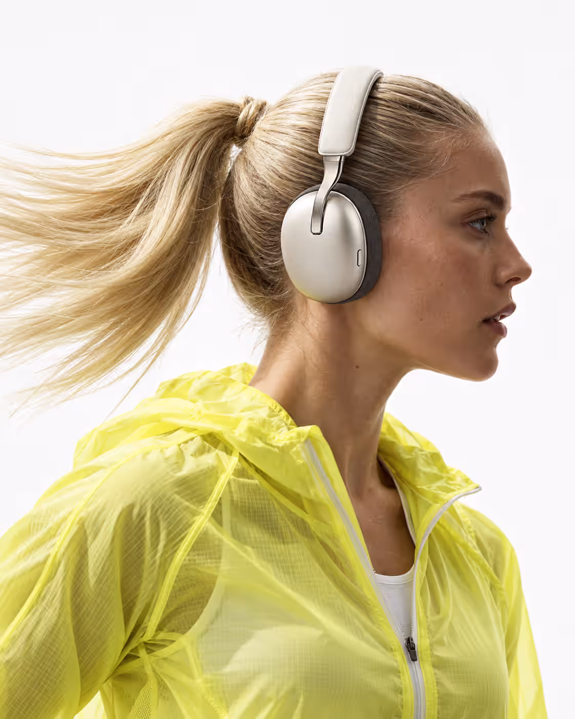 A blonde woman in a yellow running jacket wearing the headphones, ponytail swinging